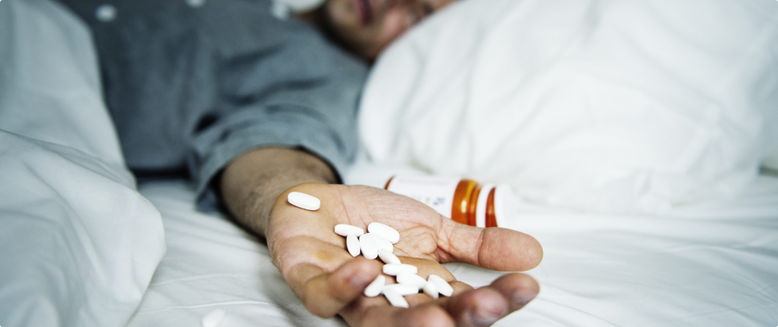 Man in bed holding hand full of white pills to the side, finding your way after losing someone you love