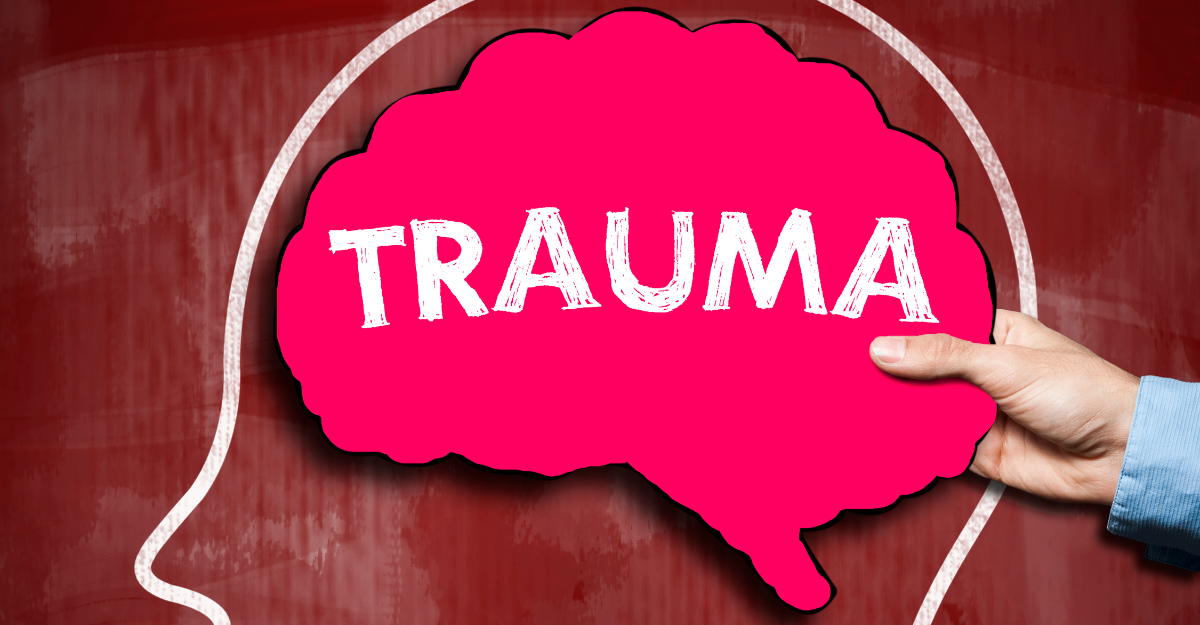 Hand holding a pink brain-shaped sign that says TRAUMA against the outline of the brain, 9 signs you need trauma therapy, iMind Mental Health Solutions