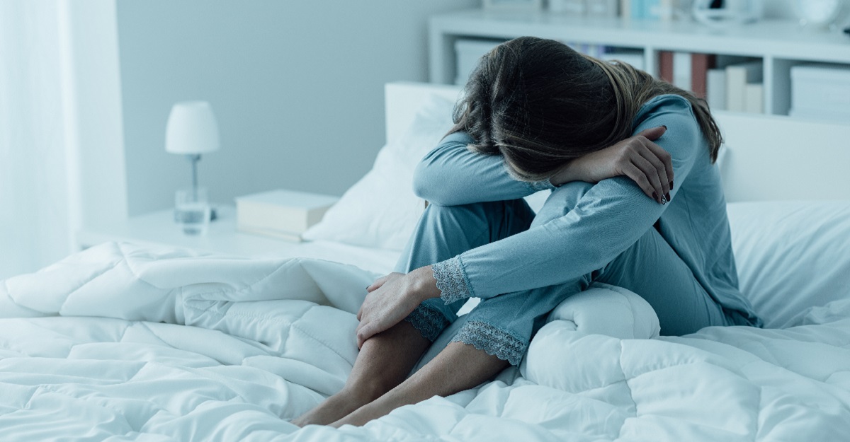 woman-with-head-down-on-her-arms-with-legs-folded-underneath-sitting-on-a-bed-what-is-situational-depression-iMind-Mental-Health-Solutions
