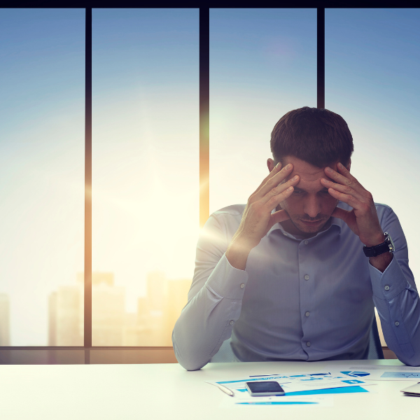 man at a conference table with head in hands in front of a window with sunlight streaming in, what is a workaholic, iMind Mental Health Solutions