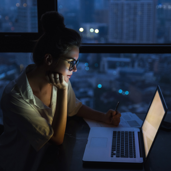 woman staring at laptop at night with a cityscape window view behind her, what is a workaholic, iMind Mental Health Solutions