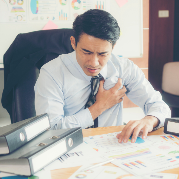 man sitting at desk clutching his heart, what is a workaholic, iMind Mental Health Solutions