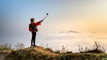 person-holding-a-selfie-stick-and-looking-at-the-phone-against-a-mountaintop-view-of-the-clouds-social-media-affect-on-mental-health-iMind-Mental-Health-Solutions
