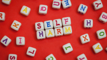 self-harm-spelled-out-in-multicolored-letters-on-small-white-blocks-social-media-affects-on-mental-health-iMind-Mental-Health-Solutions