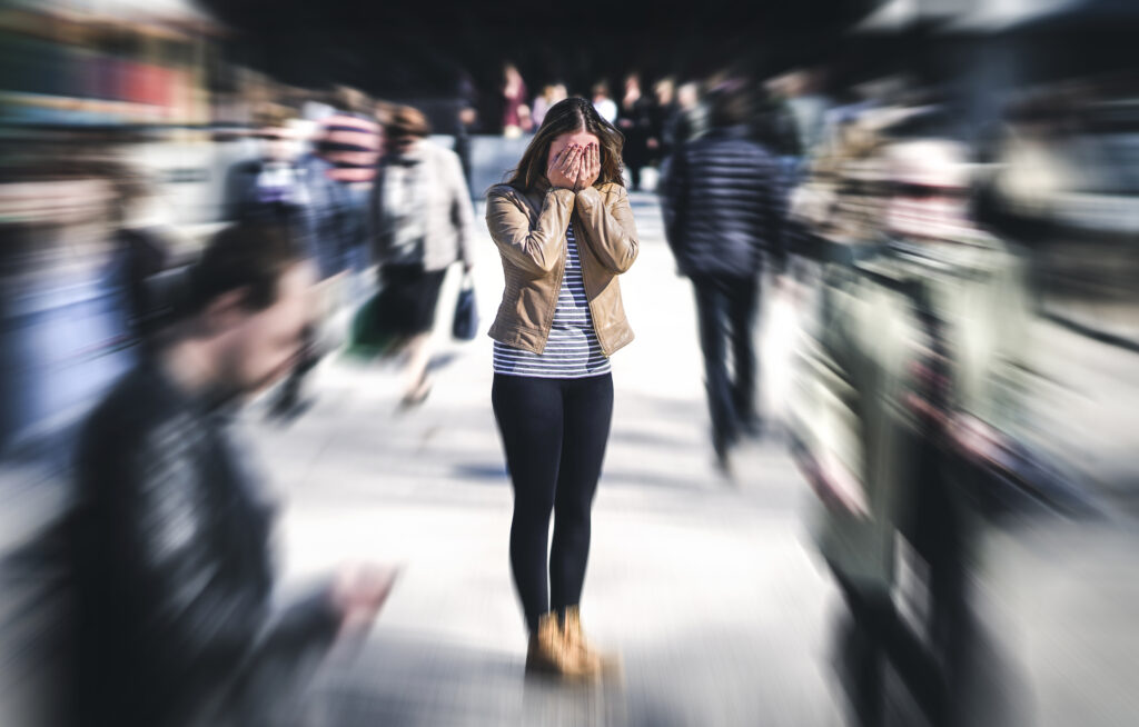 woman with hands over face in a crowd of people with the background blurred, doomscrolling, iMind Mental Health Solutions 