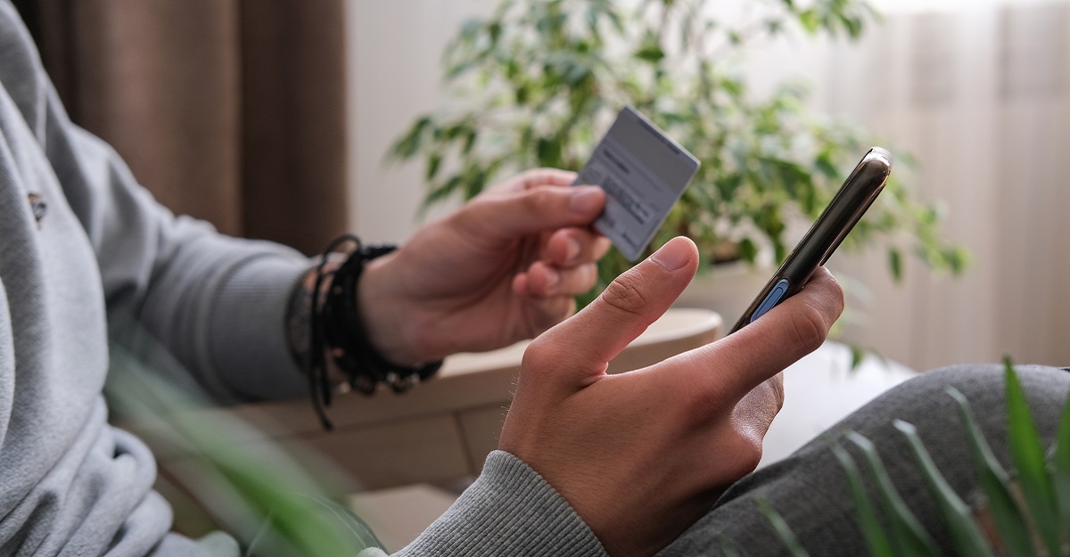 man-holding-credit-card-in-one-hand-and-cell-phone-in-another-while-sitting-on-a-couch-how-money-affects-your-mental-health-iMind-Mental-Health-Solutions