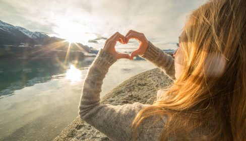 woman-looking-out-a-beach-and-mountain-landscape-with-hands-held-in-a-heart-shape-what-is-limerence-iMind-Mental-Health