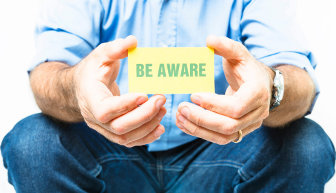 guy-in-jeans-sitting-and-holding-a-sign-that-reads-Be-Aware-what-is-catastrophizing-and-how-to-stop-it-iMind-Mental-Health-Solutions