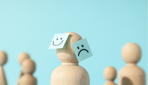 one-wooden-shaped-representation-of-a-person-in-the-foreground-with-two-small-blue-stickies-one-with-a-happy-face-and-one-with-a-frowny-face-on-the-head-passive-aggressive-port-st-lucie-stuart-iMind Mental Health