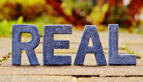 the-word-real-spelled-out-in-concrete-letters-on-a-brick-paved-path-with-fall-foliage-in-the-background-what-is-catastrophizing-and-how-to-stop-it-iMind-Mental-Health-Solutions