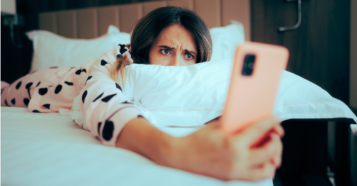 woman-laying-on-bed-looking-at-her-phone-with-an-upset-look-on-her-face-how-to-get-over-FOMO-iMind-Mental-Health-Solutions.
