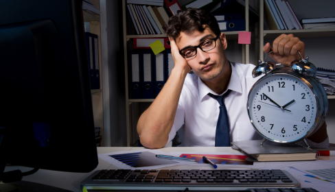 business-man-at-his-desk-at-night-looking-wearily-at-a-clock-that-reads-152-how-to-spot-a-toxic-workplace-before-you-start-iMind-Mental-Health-Solutions.
